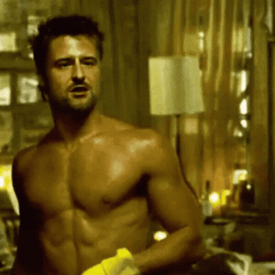 A Shirtless Man Is Holding A Yellow Towel In A Room . GIF