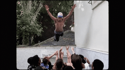 A Shirtless Man Is Jumping In The Air With His Arms Outstretched In Front Of A Crowd GIF