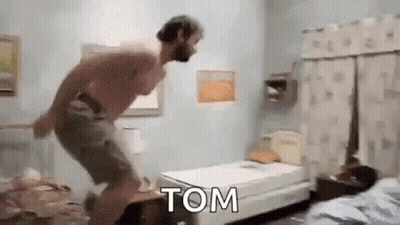 A Shirtless Man Is Jumping On A Bed In A Bedroom With The Word Tom Written On It . GIF