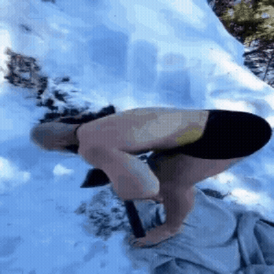 A Shirtless Man Is Kneeling Down In The Snow Holding A Hammer . GIF