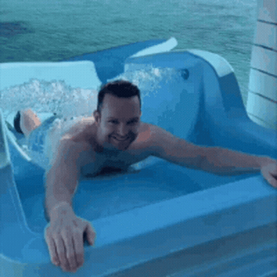 A Shirtless Man Is Laying In A Blue Tub With Water Coming Out Of It . GIF
