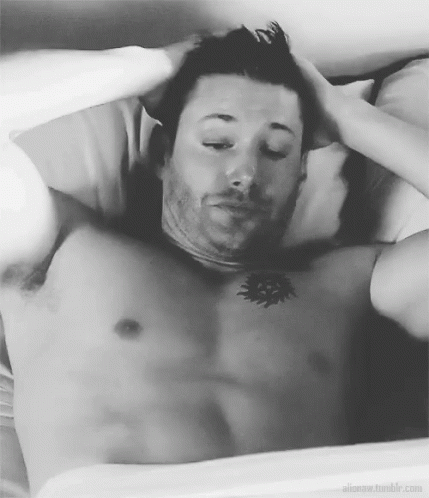 A Shirtless Man Is Laying In Bed With His Eyes Closed And His Hands On His Head . GIF