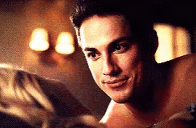 A Shirtless Man Is Laying On A Bed Looking At A Woman . GIF
