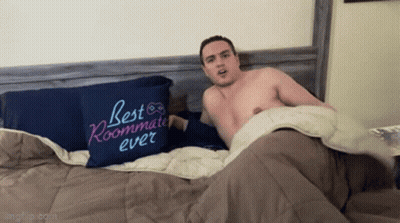 A Shirtless Man Is Laying On A Bed Next To A Pillow That Says Best Roommate Ever GIF