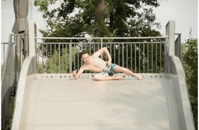 A Shirtless Man Is Laying On A Slide And Giving The Thumbs Up GIF