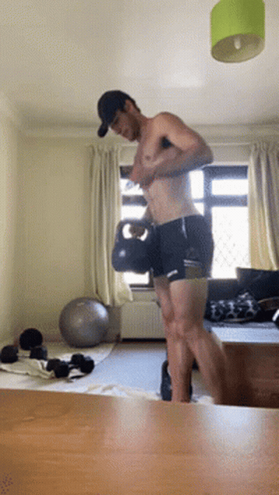 A Shirtless Man Is Lifting A Kettlebell In A Room GIF
