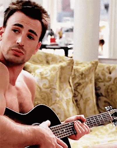 A Shirtless Man Is Playing An Acoustic Guitar On A Couch GIF