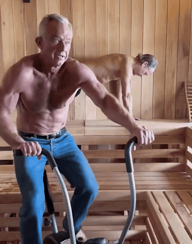 A Shirtless Man Is Riding An Exercise Bike In A Wooden Sauna GIF
