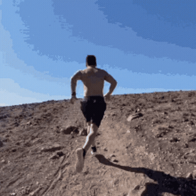 A Shirtless Man Is Running Up A Hill In The Desert GIF