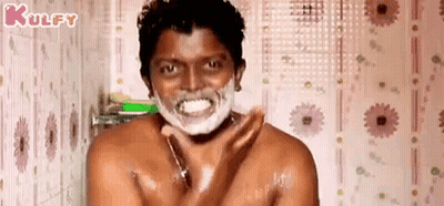 A Shirtless Man Is Shaving His Face In A Bathroom With Foam On His Face . GIF
