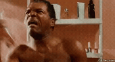 A Shirtless Man Is Shaving His Face In Front Of A Mirror In A Bathroom . GIF