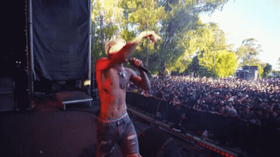 A Shirtless Man Is Singing Into A Microphone At A Concert GIF