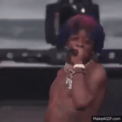 A Shirtless Man Is Singing Into A Microphone On A Stage . GIF
