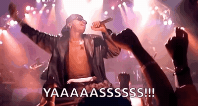 A Shirtless Man Is Singing Into A Microphone On A Stage While A Crowd Watches . GIF