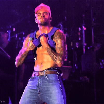 A Shirtless Man Is Singing Into A Microphone While Wearing A Hat GIF