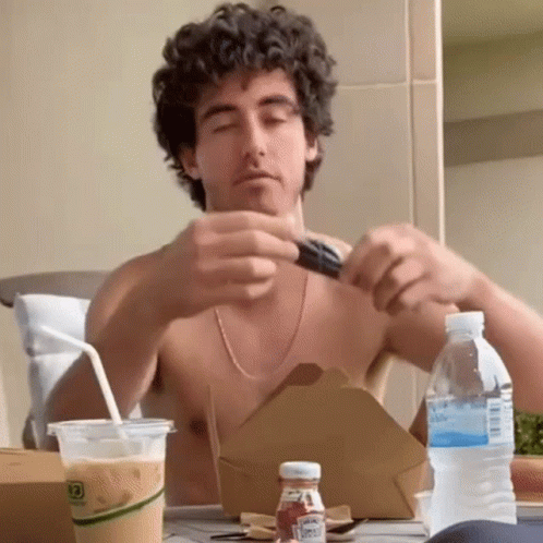 A Shirtless Man Is Sitting At A Table With A Bottle Of Ketchup And A Bottle Of Water GIF