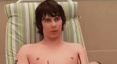 A Shirtless Man Is Sitting In A Chair With Sunglasses On . GIF