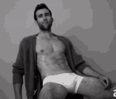A Shirtless Man Is Sitting On A Chair With His Legs Crossed . GIF