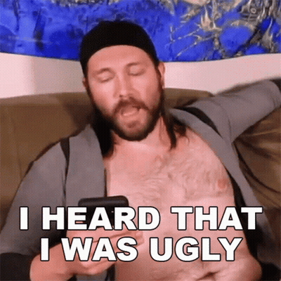 A Shirtless Man Is Sitting On A Couch Holding A Cell Phone And Says I Heard That I Was Ugly GIF