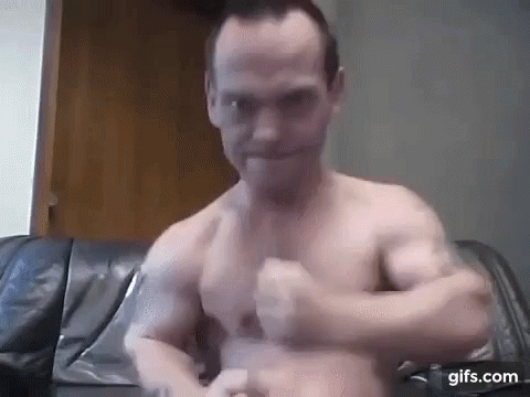 A Shirtless Man Is Sitting On A Couch With His Arms Outstretched And Looking At The Camera . GIF