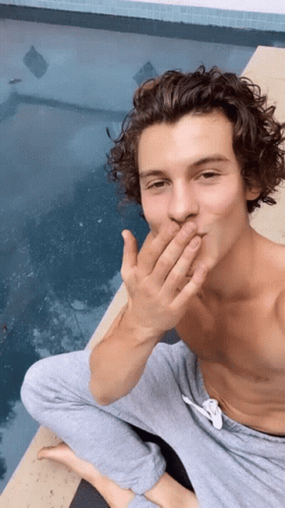 A Shirtless Man Is Sitting On The Edge Of A Pool Covering His Mouth With His Hand . GIF