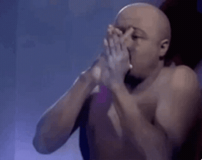 A Shirtless Man Is Smoking A Cigarette And Blowing Smoke Into His Mouth . GIF