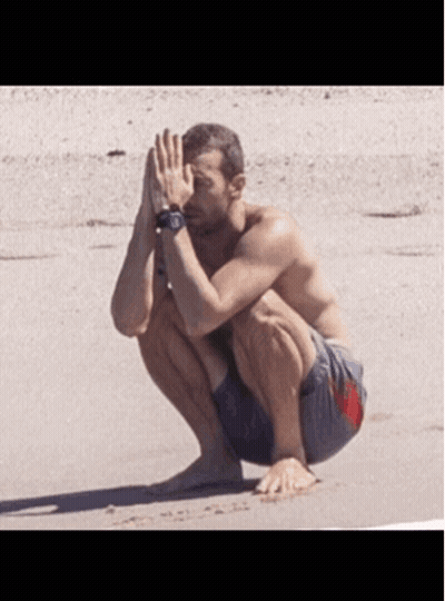 A Shirtless Man Is Squatting Down On The Beach GIF