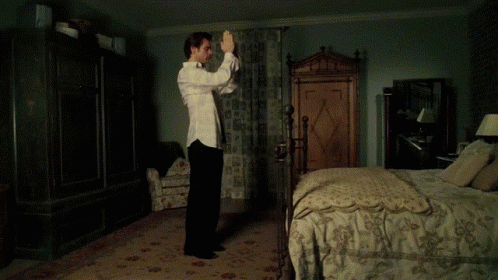 A Shirtless Man Is Standing In A Bedroom With A Bed GIF