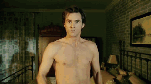A Shirtless Man Is Standing In A Bedroom With A Picture On The Wall GIF