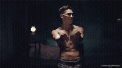 A Shirtless Man Is Standing In A Dark Room With His Arms Outstretched . GIF