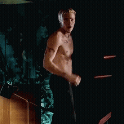 A Shirtless Man Is Standing In A Dark Room With His Hand In His Hair . GIF