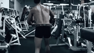 A Shirtless Man Is Standing In A Gym With A Bunch Of Exercise Equipment . GIF