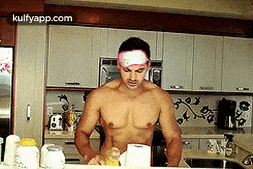 A Shirtless Man Is Standing In A Kitchen With A Bandage On His Forehead . GIF
