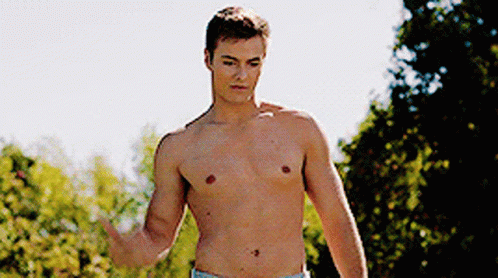 A Shirtless Man Is Standing In A Park With His Hand Outstretched GIF