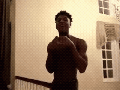 A Shirtless Man Is Standing In A Room With His Hands In The Air . GIF