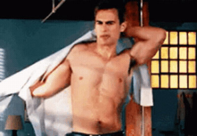 A Shirtless Man Is Standing In A Room With His Shirt Off . GIF