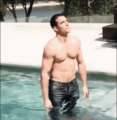 A Shirtless Man Is Standing In A Swimming Pool Wearing Wet Jeans . GIF