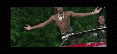 A Shirtless Man Is Standing In Front Of A Car With His Arms Outstretched And A Bandana On His Head . GIF