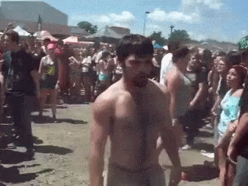 A Shirtless Man Is Standing In Front Of A Crowd At A Festival . GIF