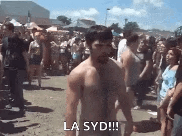 A Shirtless Man Is Standing In Front Of A Crowd At A Music Festival . GIF