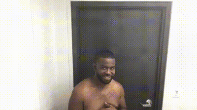 A Shirtless Man Is Standing In Front Of A Door With His Hands On His Chest . GIF