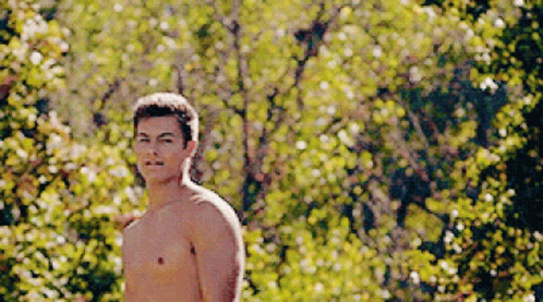 A Shirtless Man Is Standing In Front Of A Forest Of Trees GIF