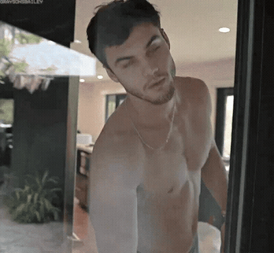 A Shirtless Man Is Standing In Front Of A Glass Door . GIF