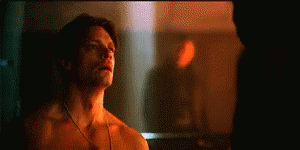 A Shirtless Man Is Standing In Front Of A Mirror And Looking At Himself . GIF