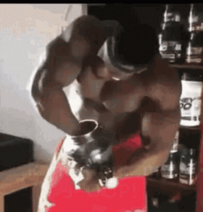 A Shirtless Man Is Standing In Front Of A Shelf With Bottles Of Protein . GIF