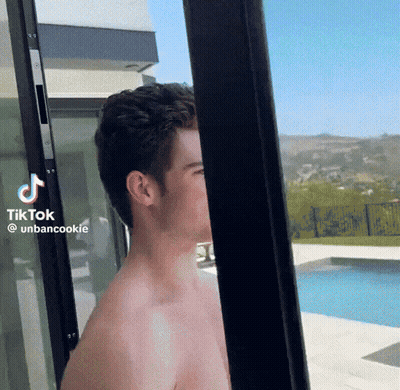 A Shirtless Man Is Standing In Front Of A Sliding Glass Door With Tiktok Written On The Bottom Right Corner GIF