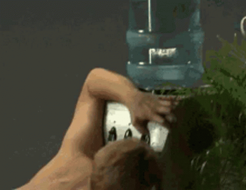 A Shirtless Man Is Standing In Front Of A Water Cooler . GIF