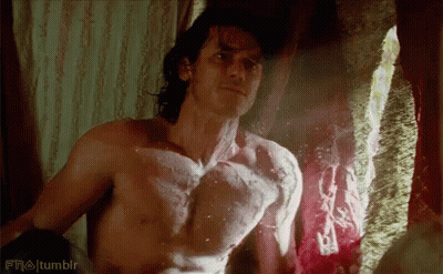 A Shirtless Man Is Standing In Front Of A Window And Looking At Himself . GIF