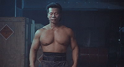 A Shirtless Man Is Standing In Front Of A Wooden Crate In A Dark Room . GIF