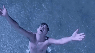A Shirtless Man Is Standing In The Rain With His Arms Outstretched In The Air . GIF